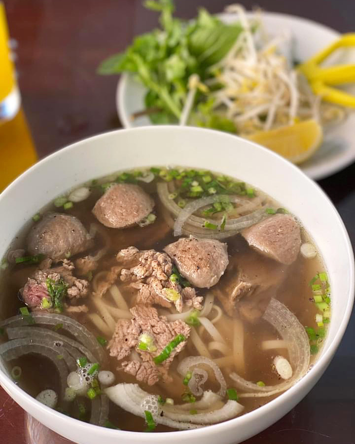 En ångande skål pho serverad med färska vietnamesiska örter